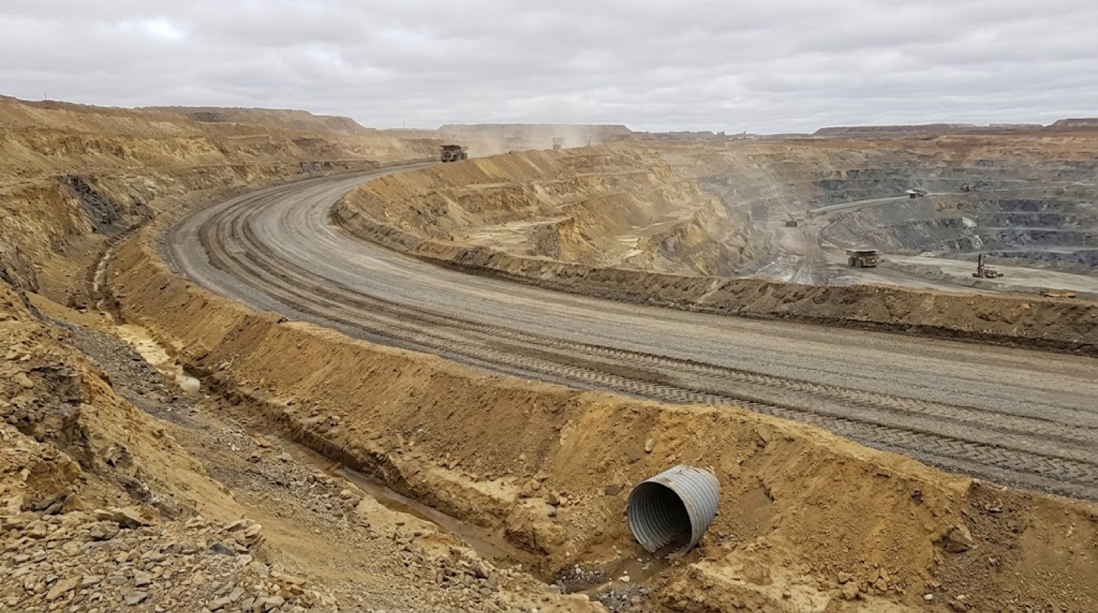 A gravel haul road curving through an open-pit mine, with berms and a culvert